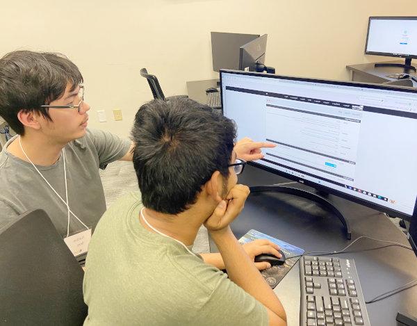 Two students pointing to a laptop in a classroom setting.